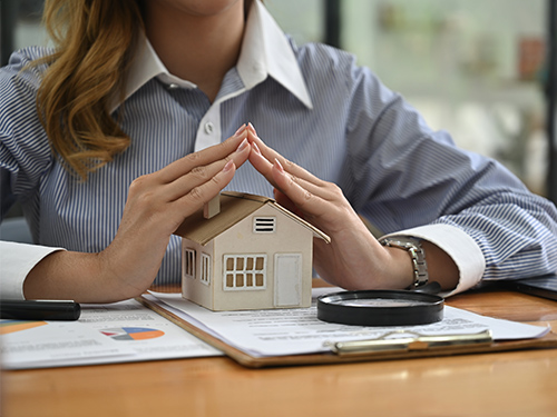 Woman with hands shielding miniature model home, symbolizing roof warranty coverage.